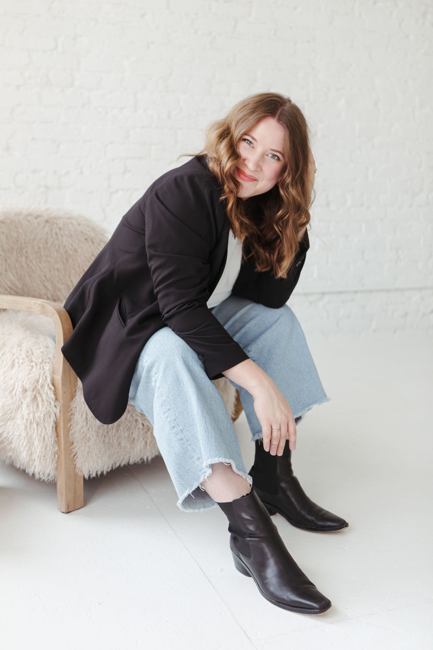 Casual fashion look with light wash jeans and black ankle boots shown in multiple relaxed sitting poses against white wall.