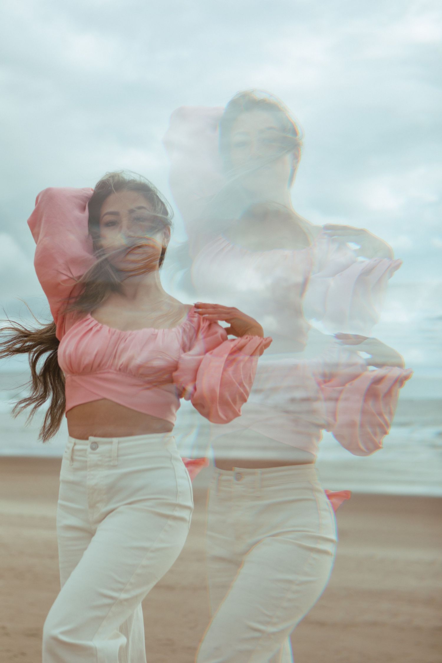 Double exposure photo of dancers in pink tops and white pants moving gracefully on a beach.