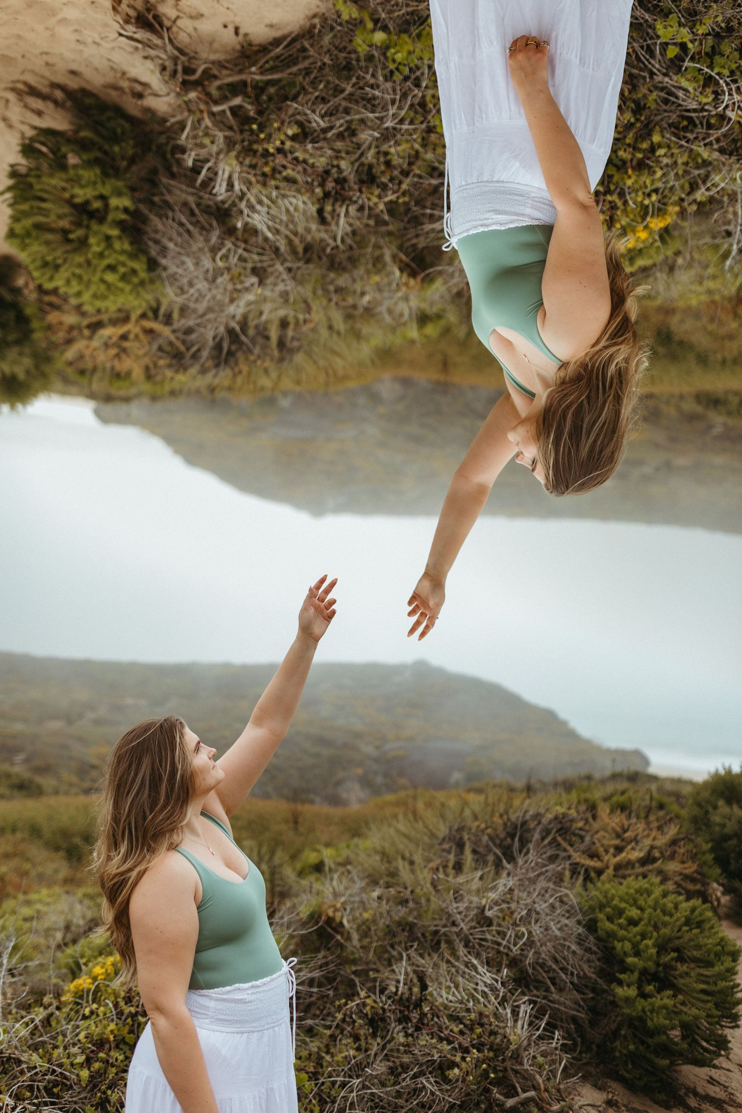 Two dancers perform an artistic aerial move in a natural outdoor setting with a misty lake backdrop.