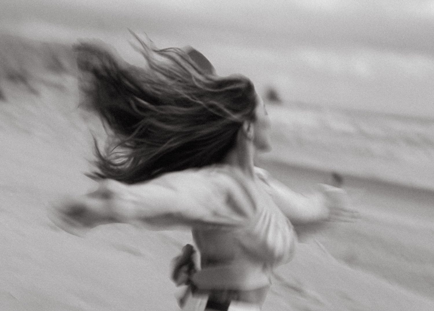 A blurred black and white motion photograph of someone spinning at the beach with hair flowing in the wind.
