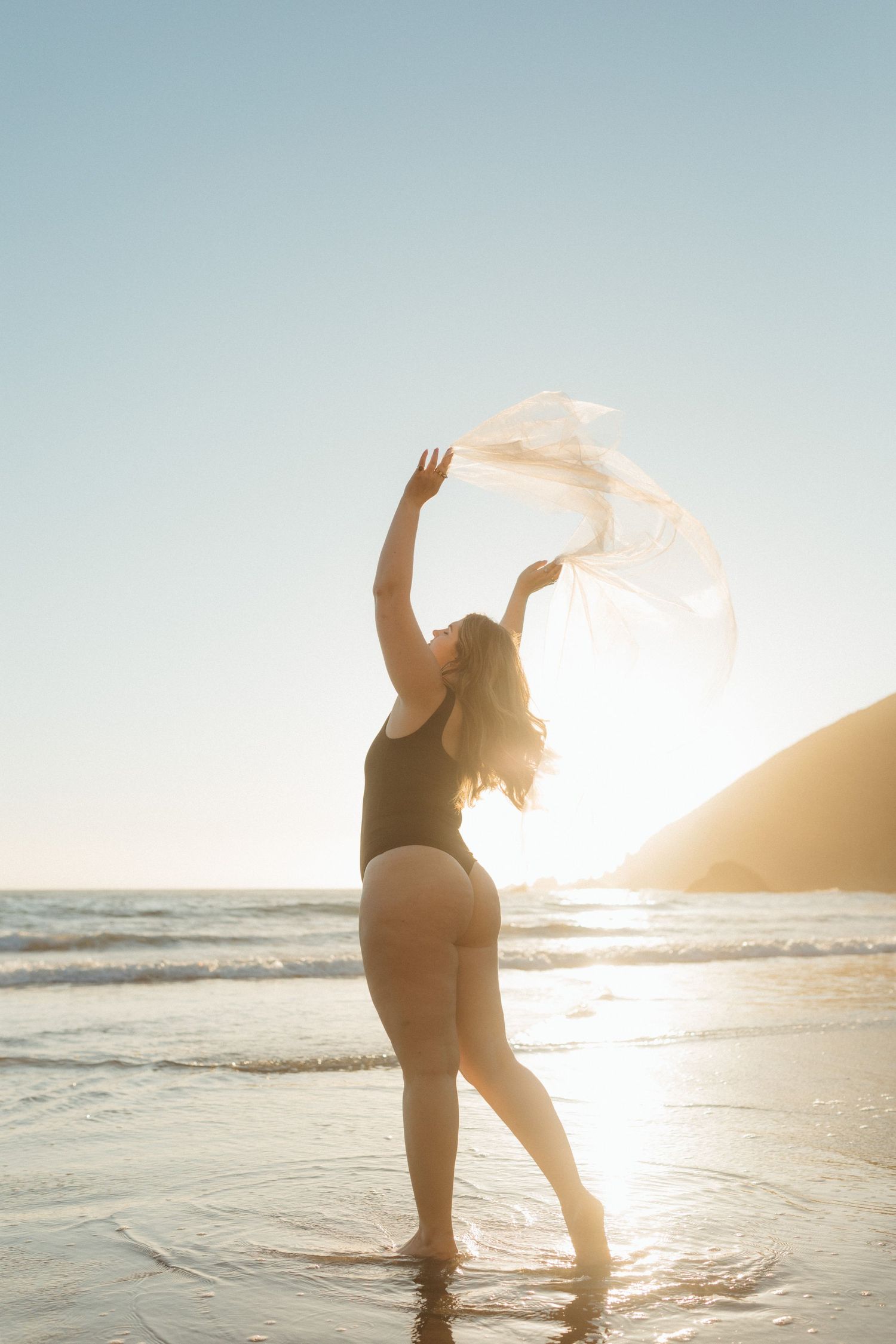 Person in black swimwear dances gracefully in ocean waves during golden hour, fabric flowing in sea breeze.