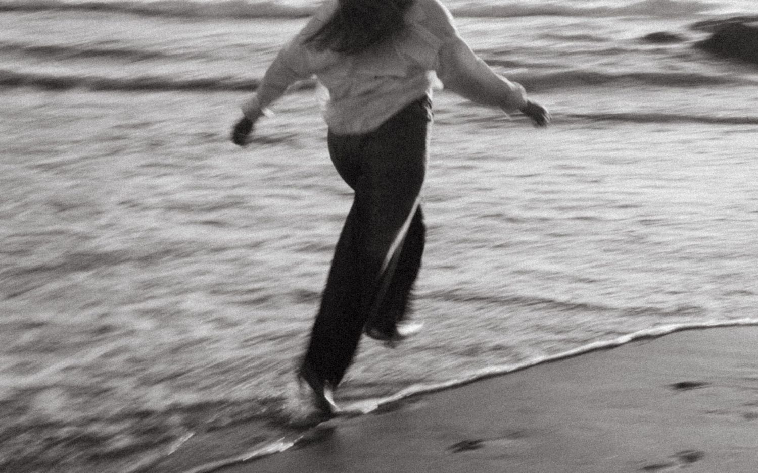 Black and white photo of people walking along a foggy beach shoreline with waves rolling in.