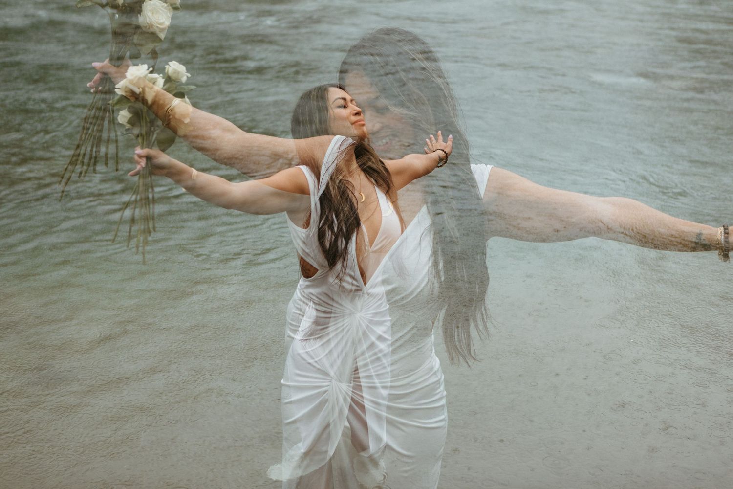 A person in a flowing white dress dances gracefully in shallow water, creating ripples and splashes in the sunlight.