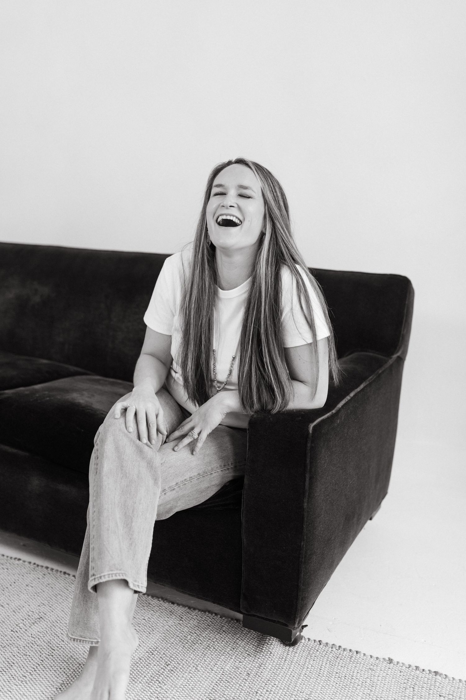 Black and white photo series showing joyful laughter while sitting on a dark couch against white background.