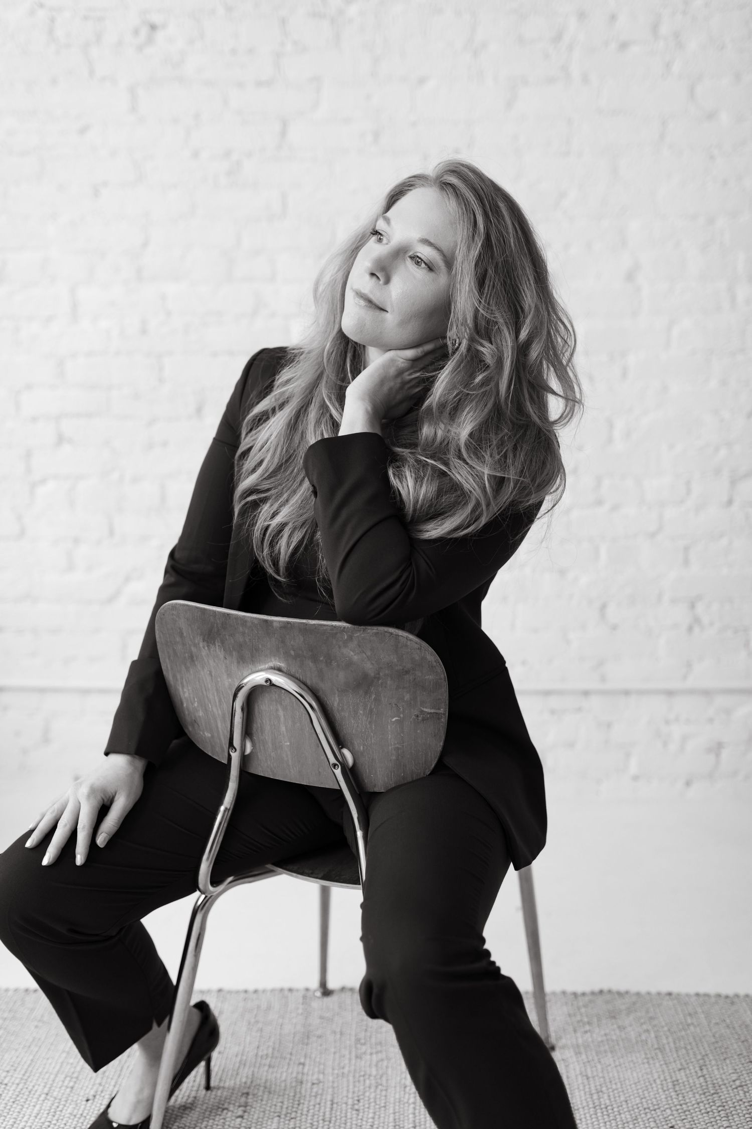black and white photo showing a woman sitting in a chair posing with her left arm up and left hand under her chin