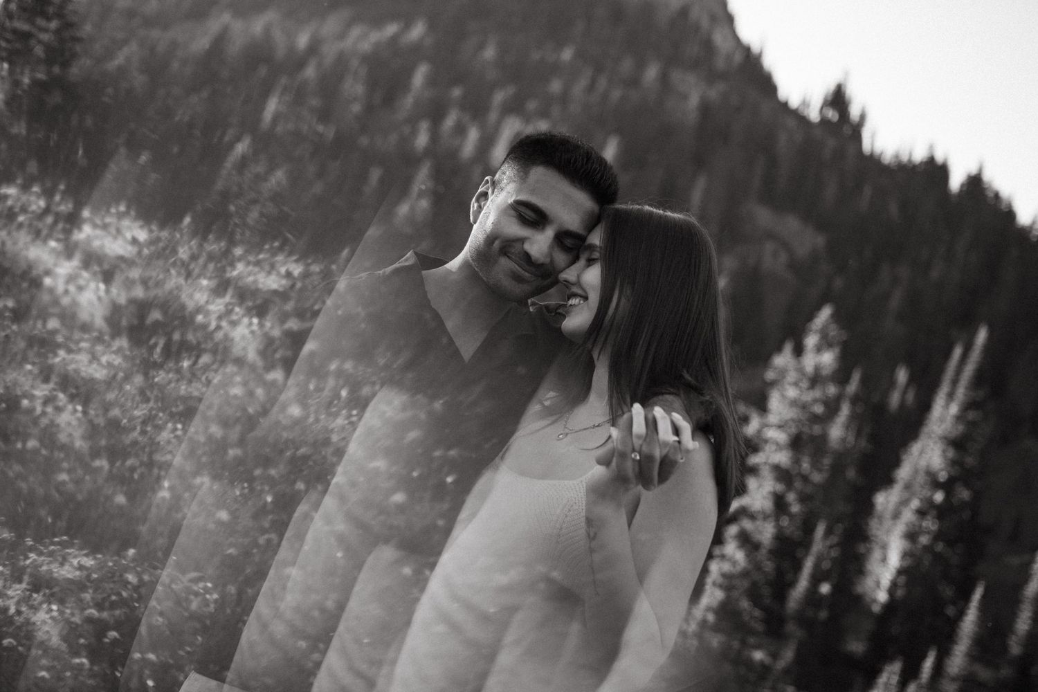 Black and white image of couples in an intimate moment against a mountainous forest backdrop.