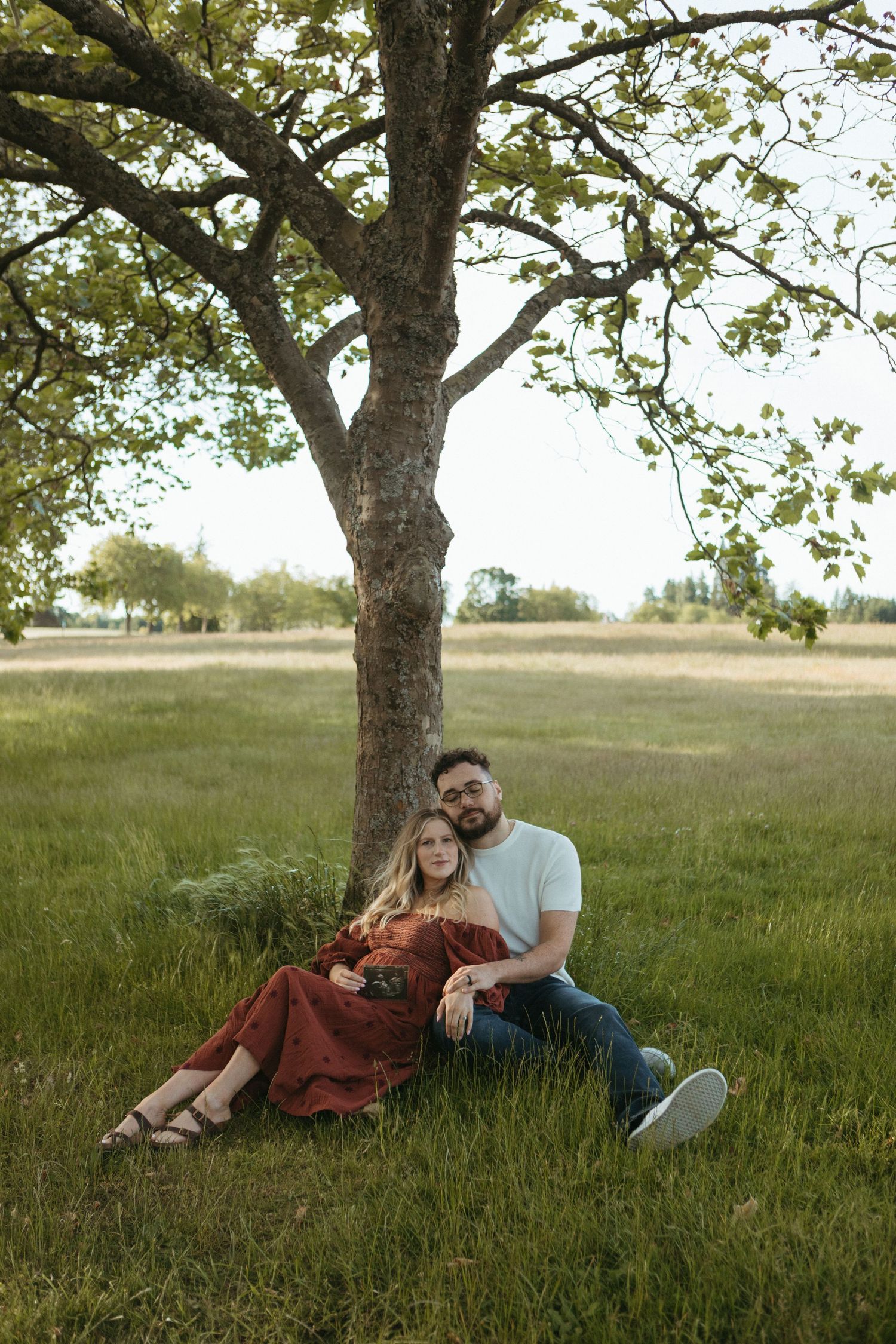 Romantic couple relaxing together under a large tree in a sunlit meadow.