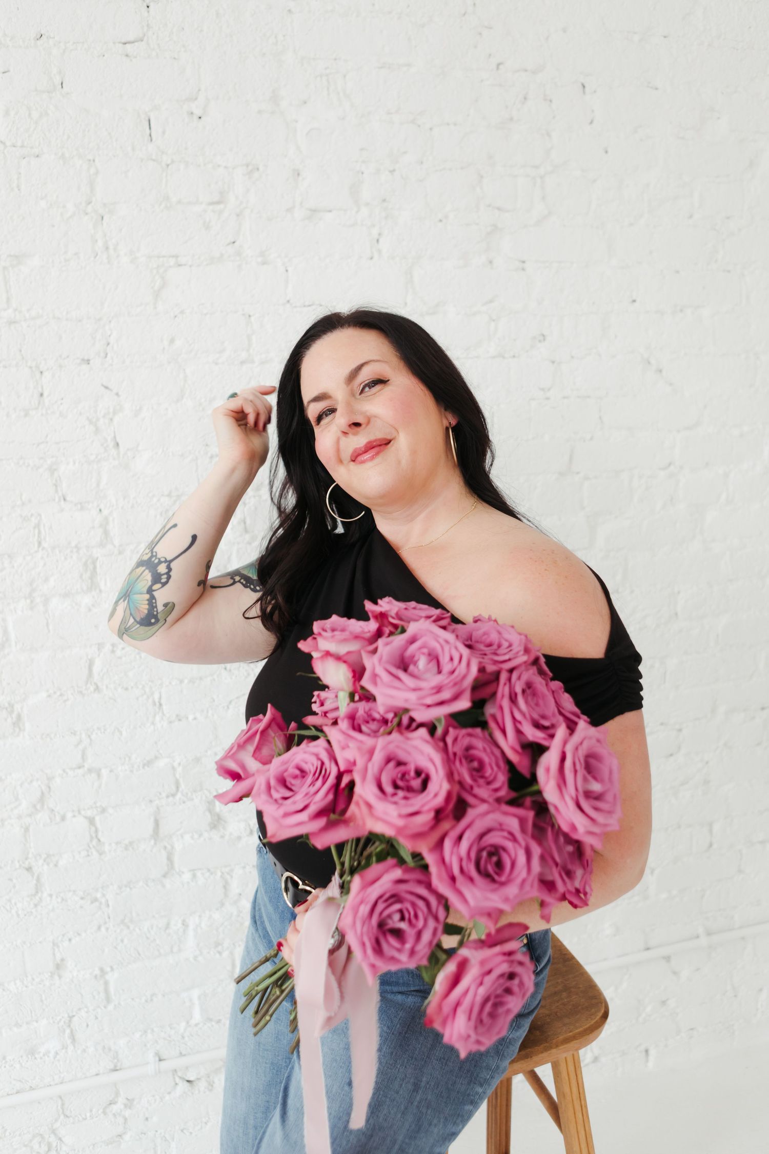 Woman in jeans holding vibrant pink roses against white wall in casual lifestyle photoshoot.