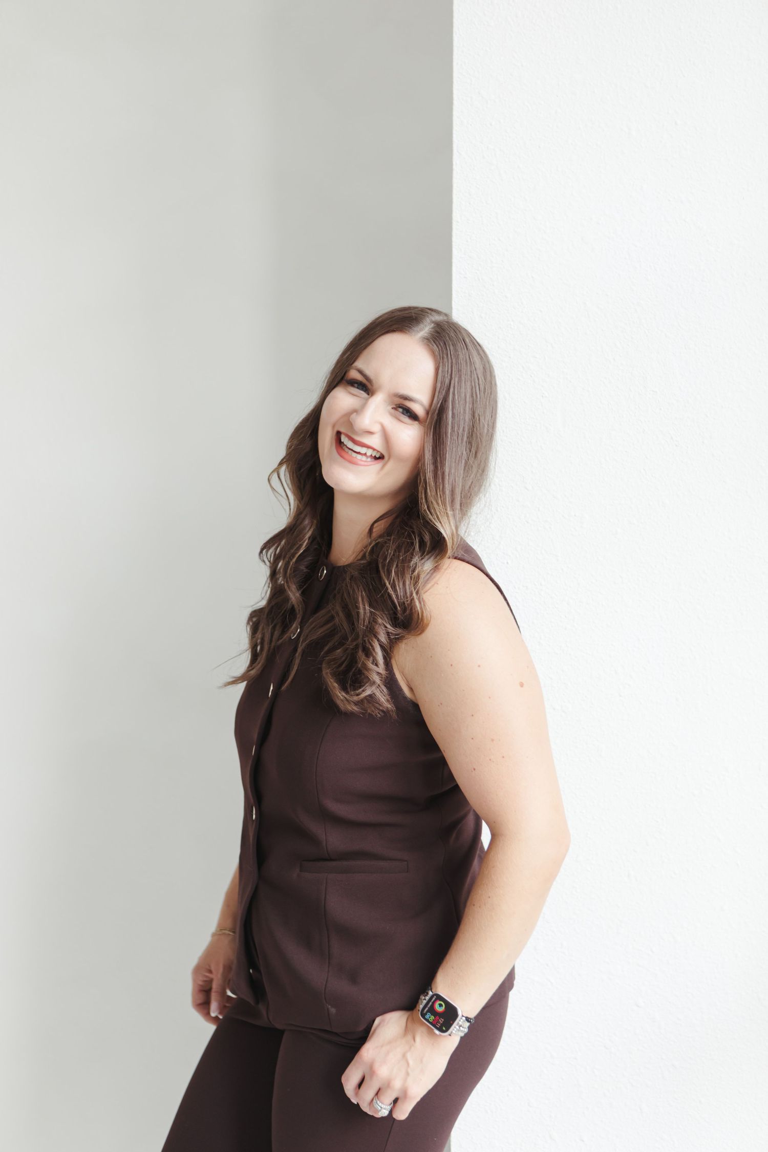 Woman in brown sleeveless dress poses against white background with joyful expression.