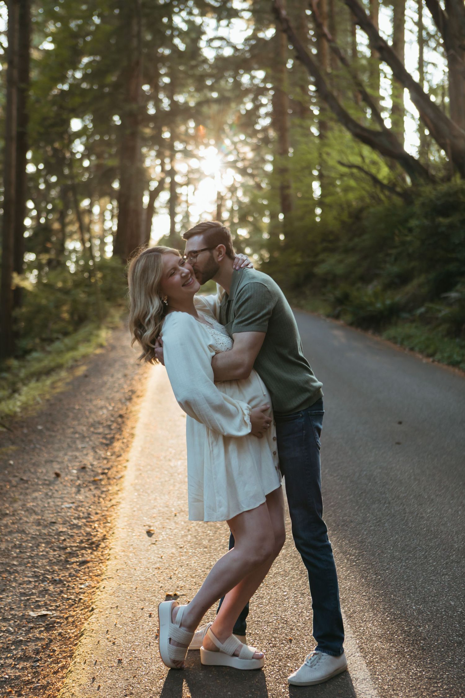 A couple embraces lovingly on a sunlit forest path during golden hour.
