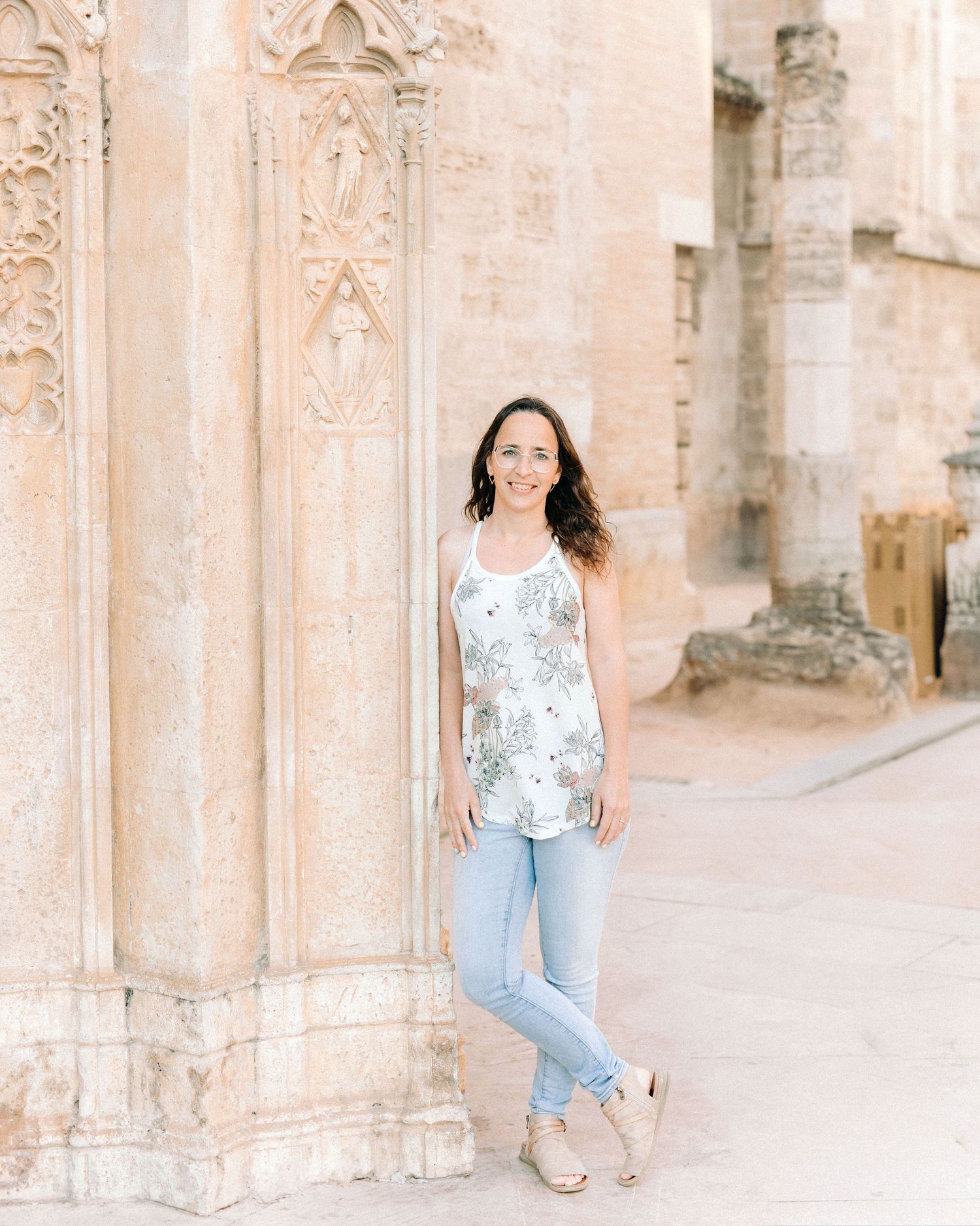 A person in light jeans and floral tank top poses against an ornate stone church exterior with gothic architectural details.