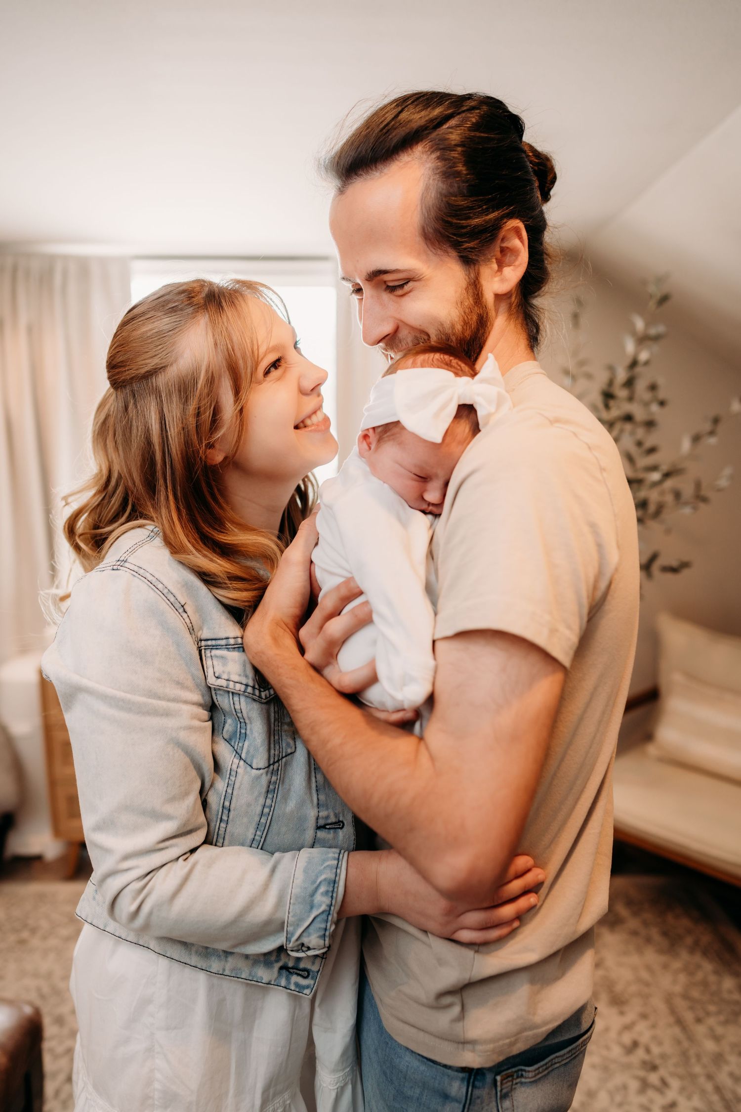 A couple sharing a tender moment while holding their newborn baby in a warmly lit home setting.