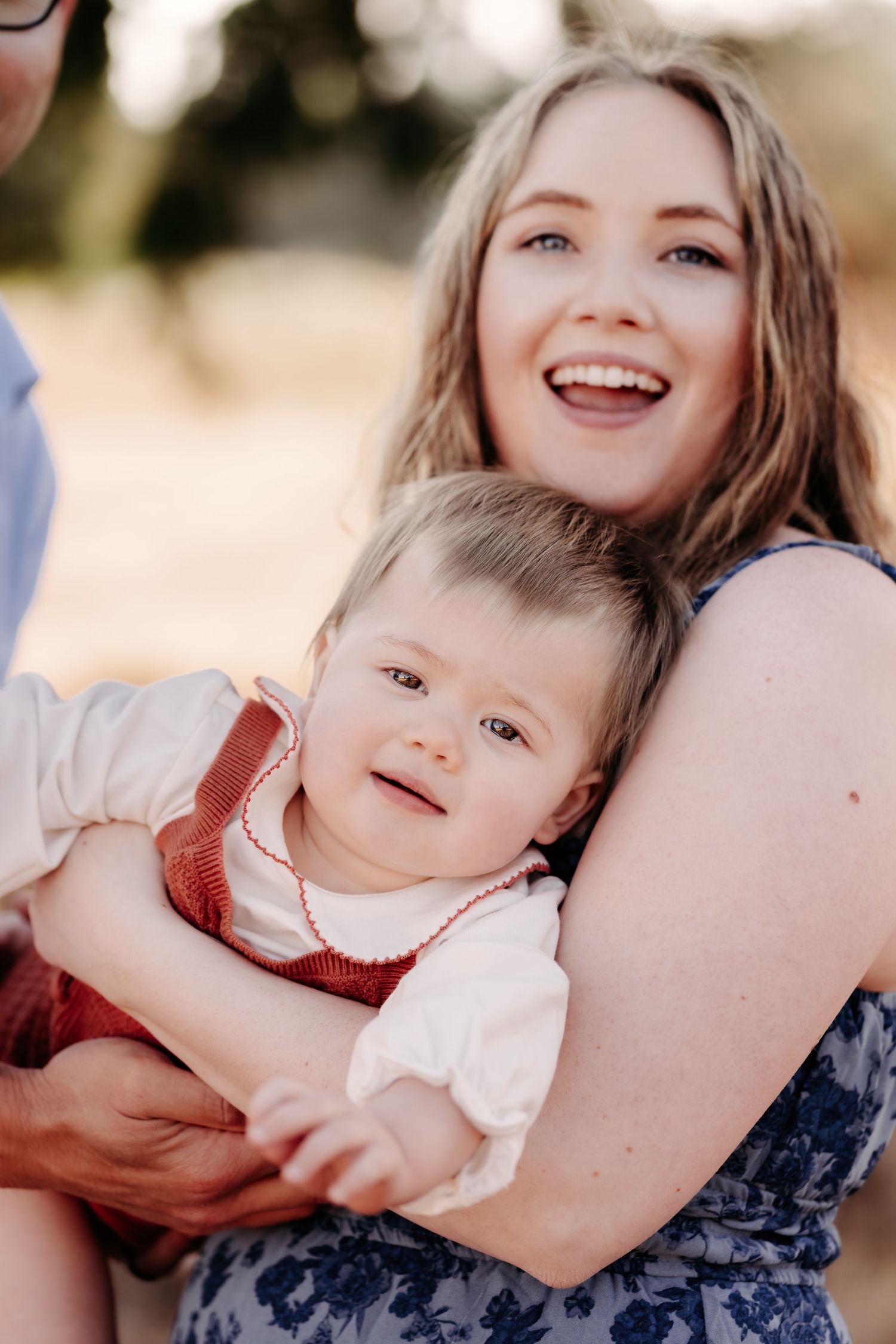 Laughing young mother holding her baby in a red outfit outdoors in warm golden light during family photo session in Puyallup, Wa.