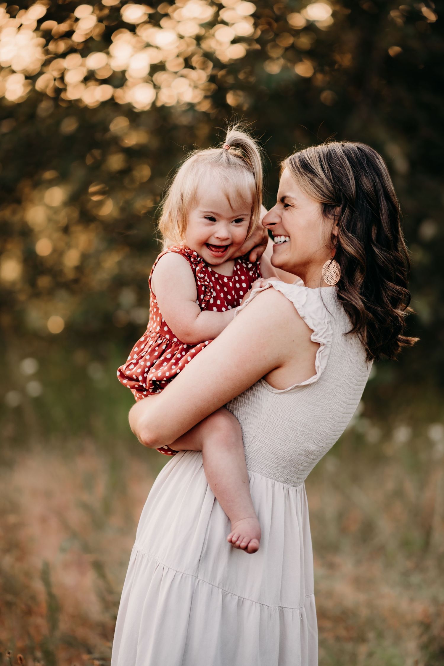 A smiling mother in a white dress holds her laughing toddler girl in a red polka dot dress during golden hour photo session in Puyallup, Wa.