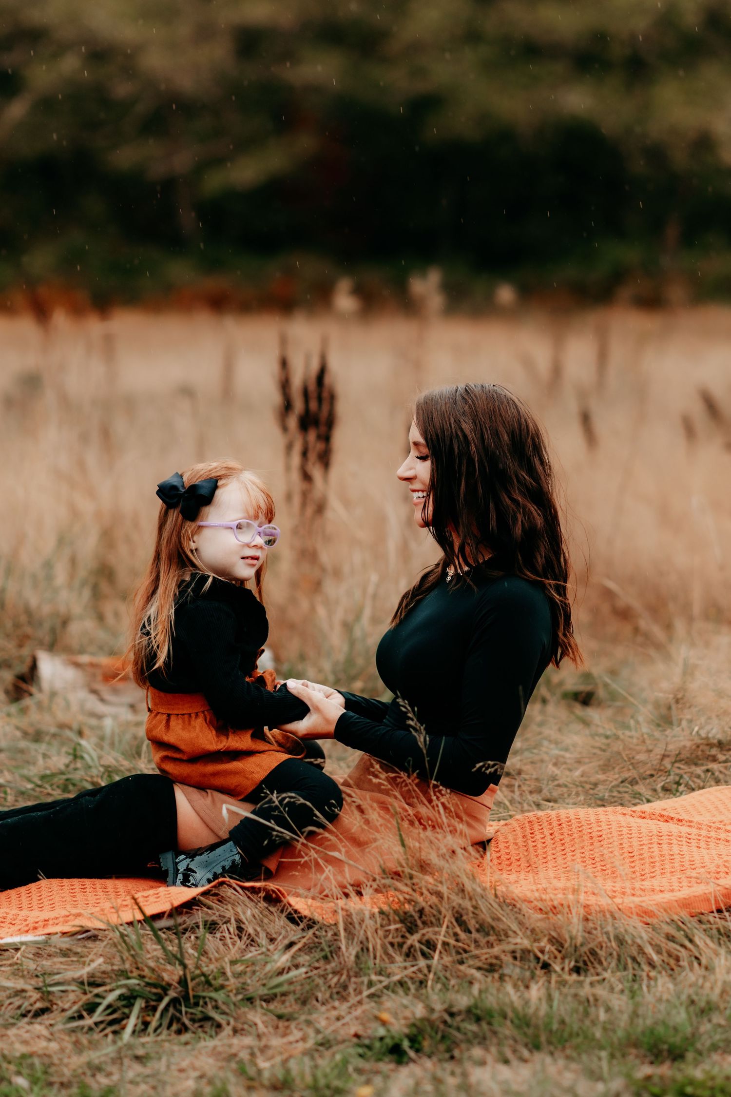 A woman and young girl sit together on an orange blanket in a field during fall family photos in Puyallup, Wa.