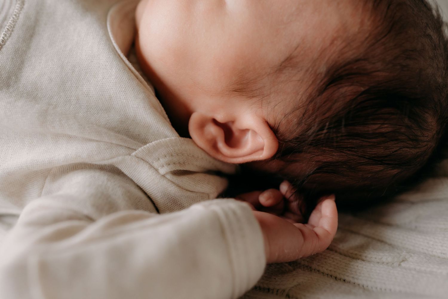 Close up view of newborn baby girl sleeping peacefully on white bedding in soft natural light during in home newborn photo session in Tacoma