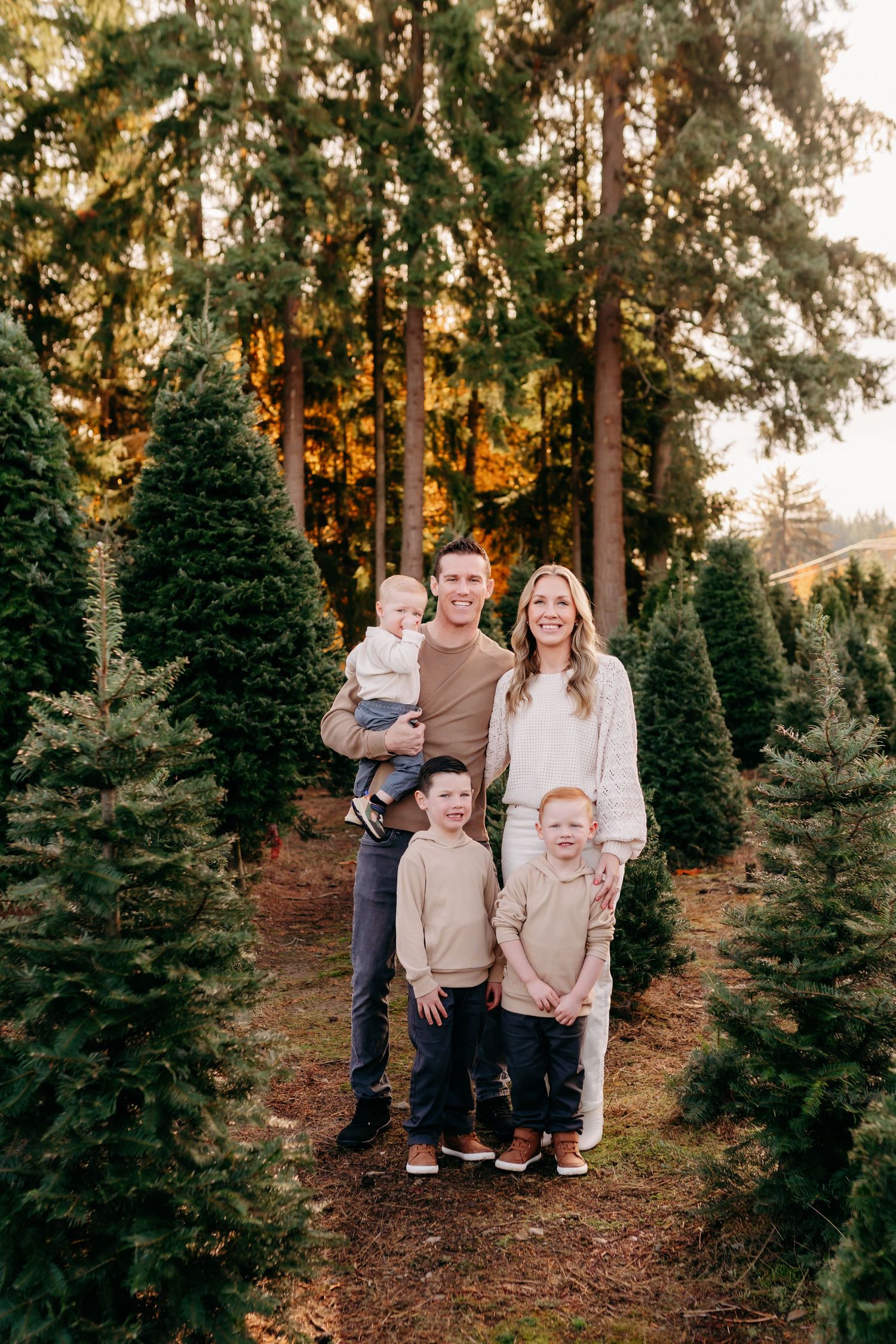 Family of five posing among green Christmas trees at a tree farm during golden hour sunset for Christmas photos in Tacoma,Wa.