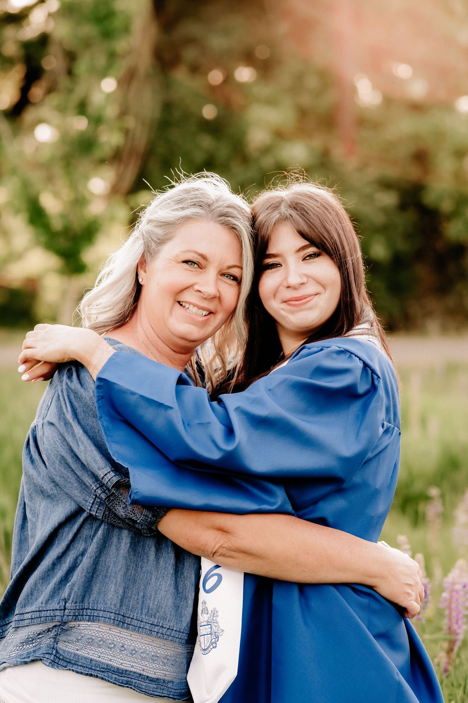A graduate in blue gown hugs an older woman outdoors, both smiling warmly during a graduation celebration.
