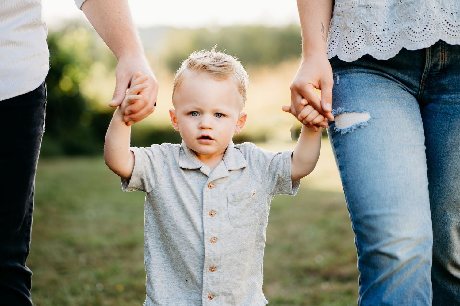 Toddler boy stand between parents holding hands and walking forward.