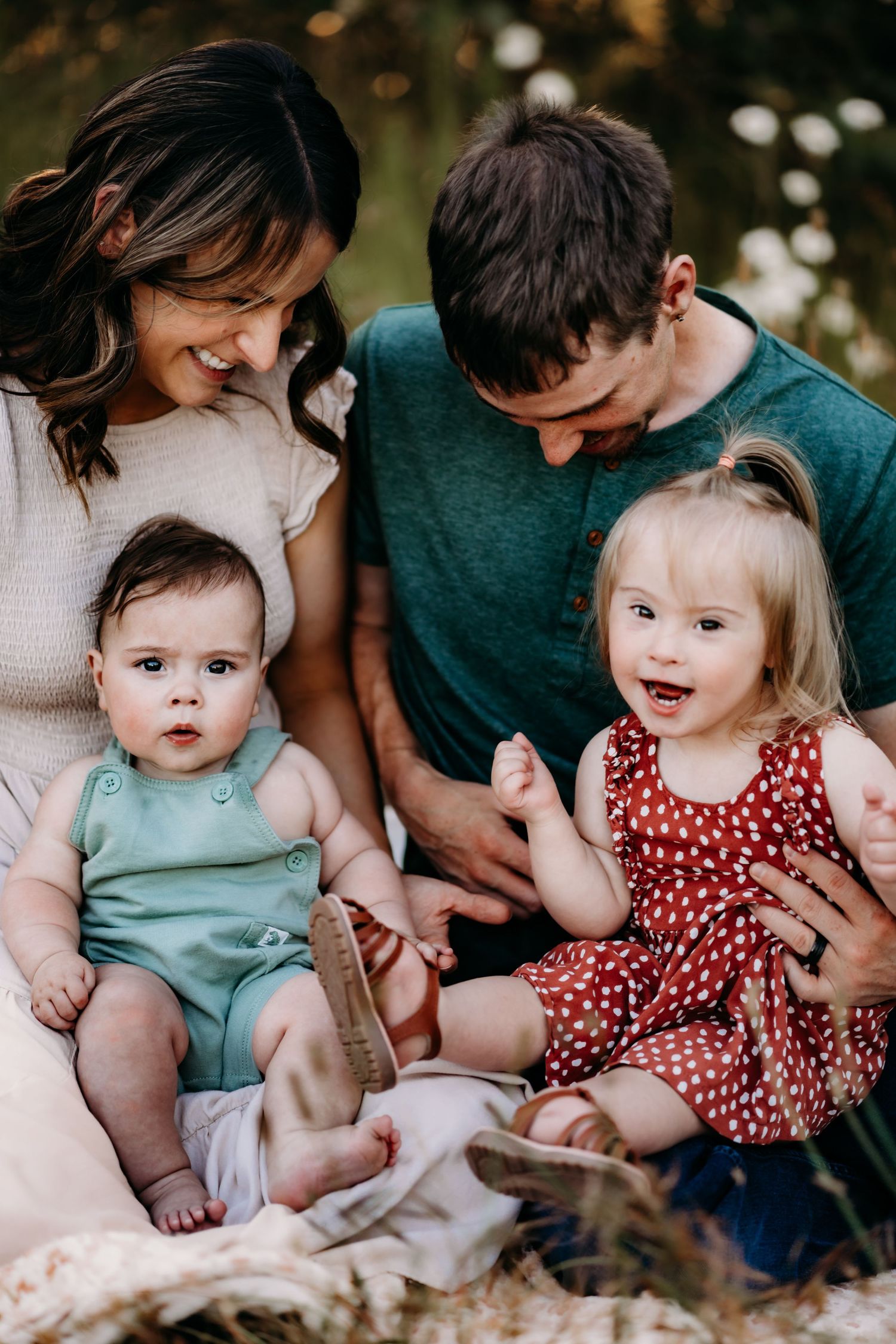 Happy family with two young children sitting outdoors on a blanket, smiling and enjoying time together during family photos in Puyallup, Wa.