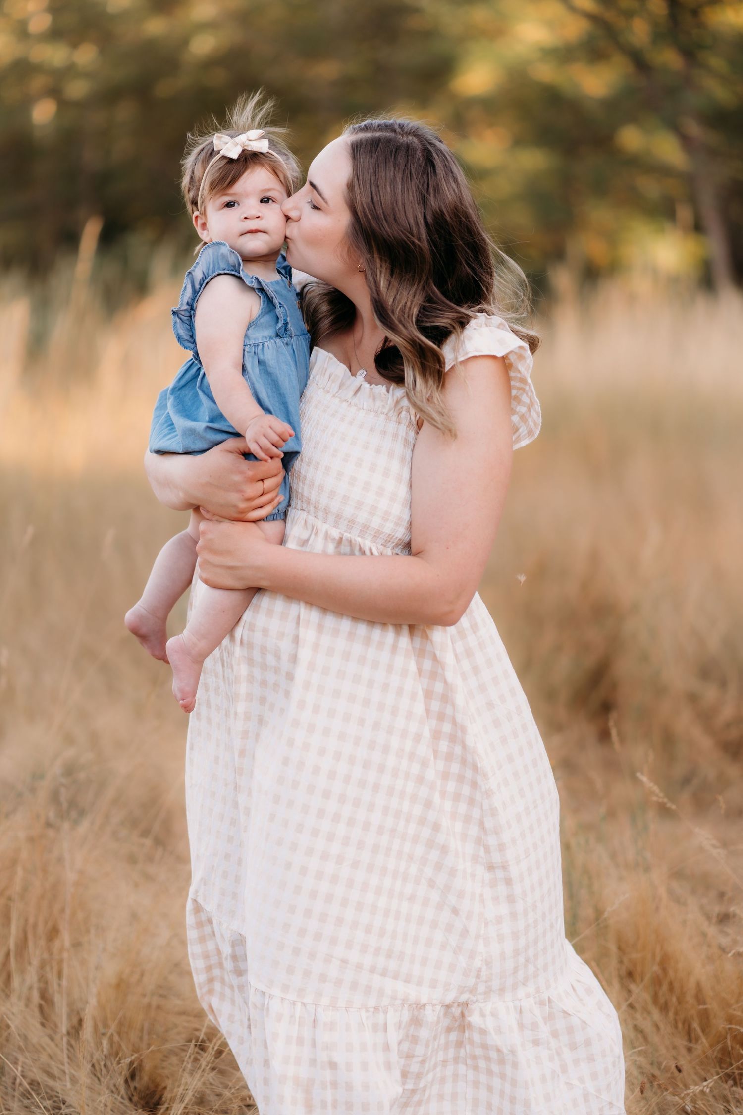 A tender moment between mom and baby girl in a sun-lit field of tall golden grass during family photos in Puyallup, Wa.