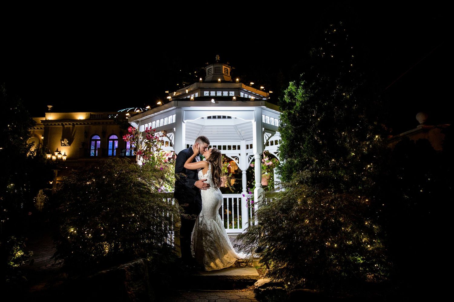 A couple shares a romantic moment in an illuminated gazebo at night.
