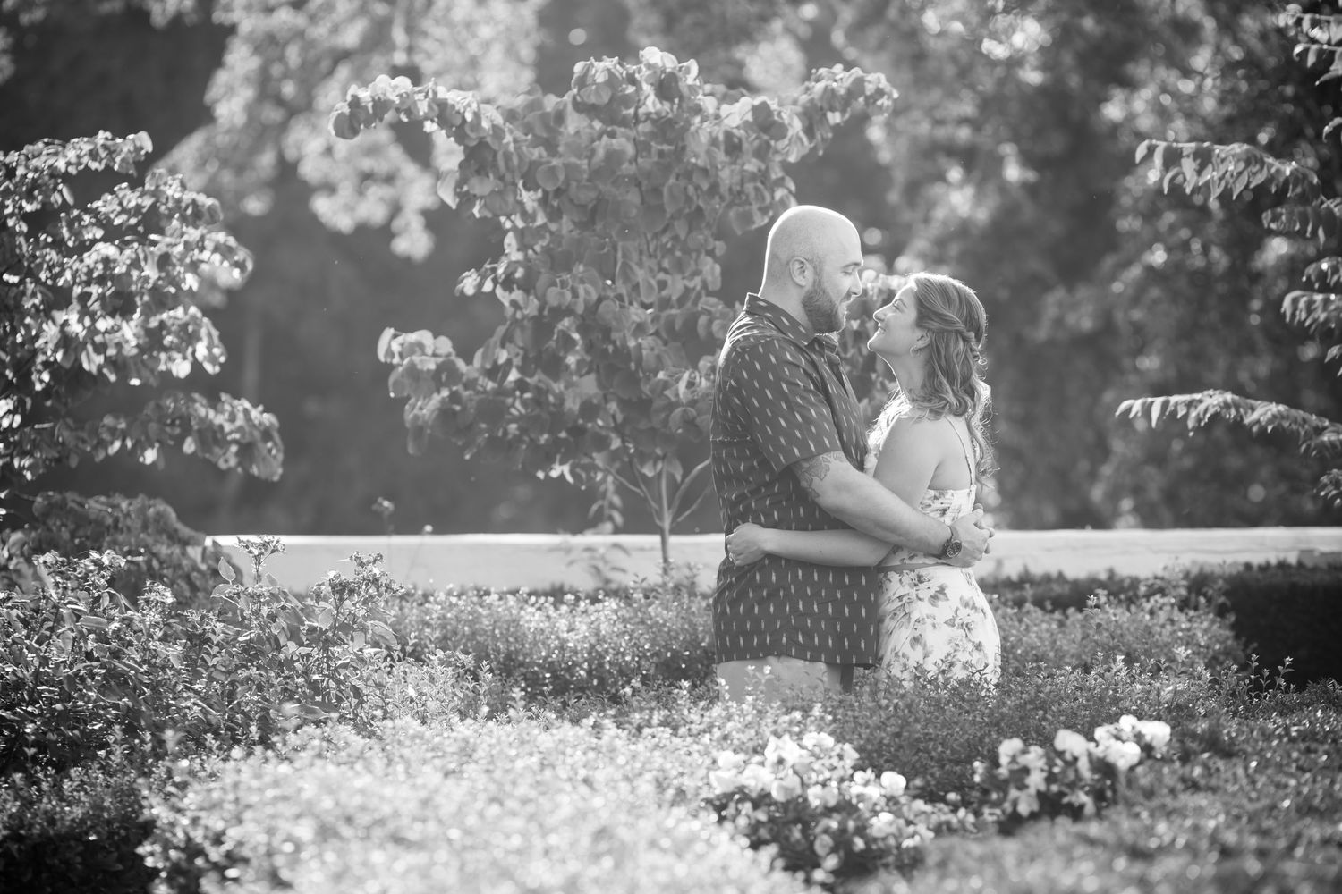A romantic black and white portrait of a couple embracing in a garden setting.