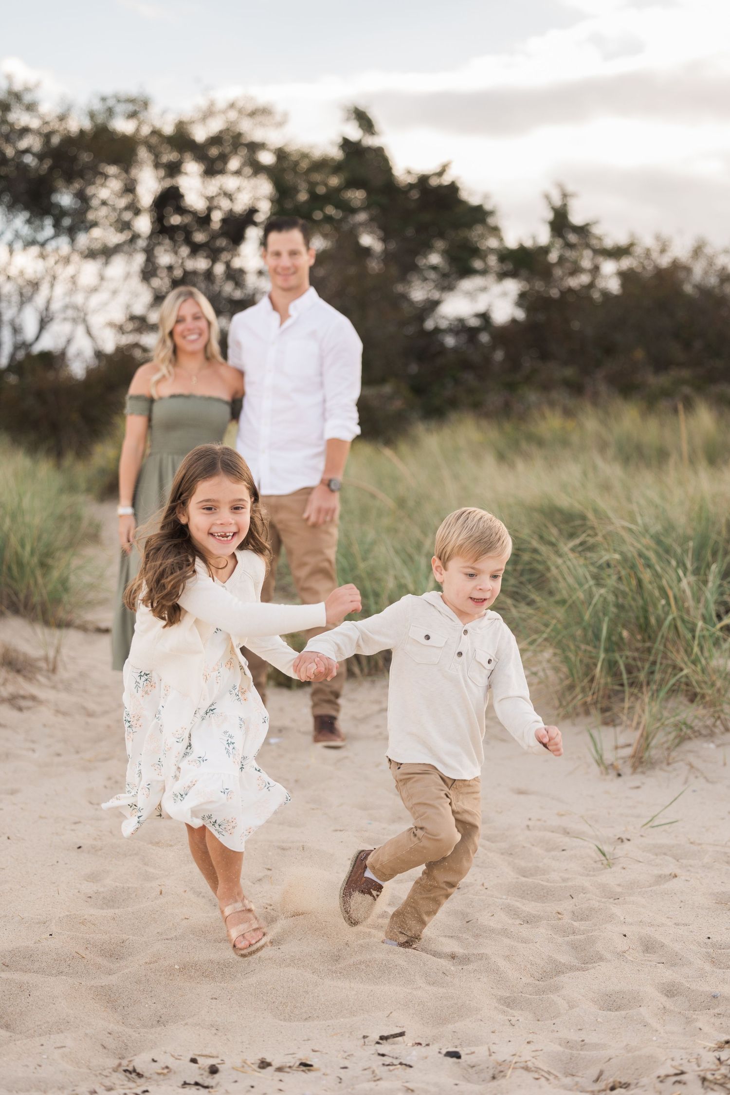 A family enjoys a playful moment on sandy beach dunes during sunset.