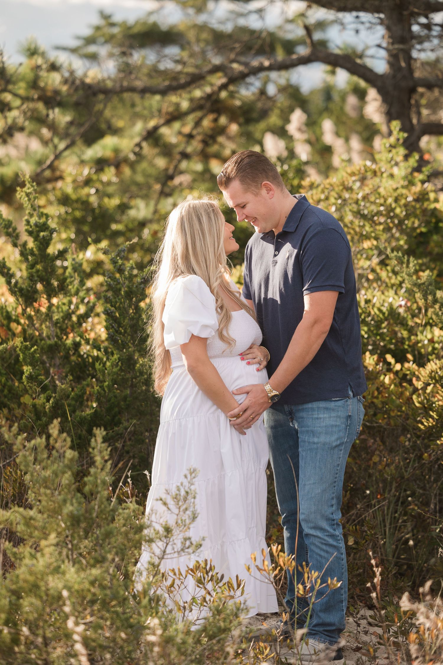 A couple shares an intimate moment in nature wearing white and navy outfits during sunset.