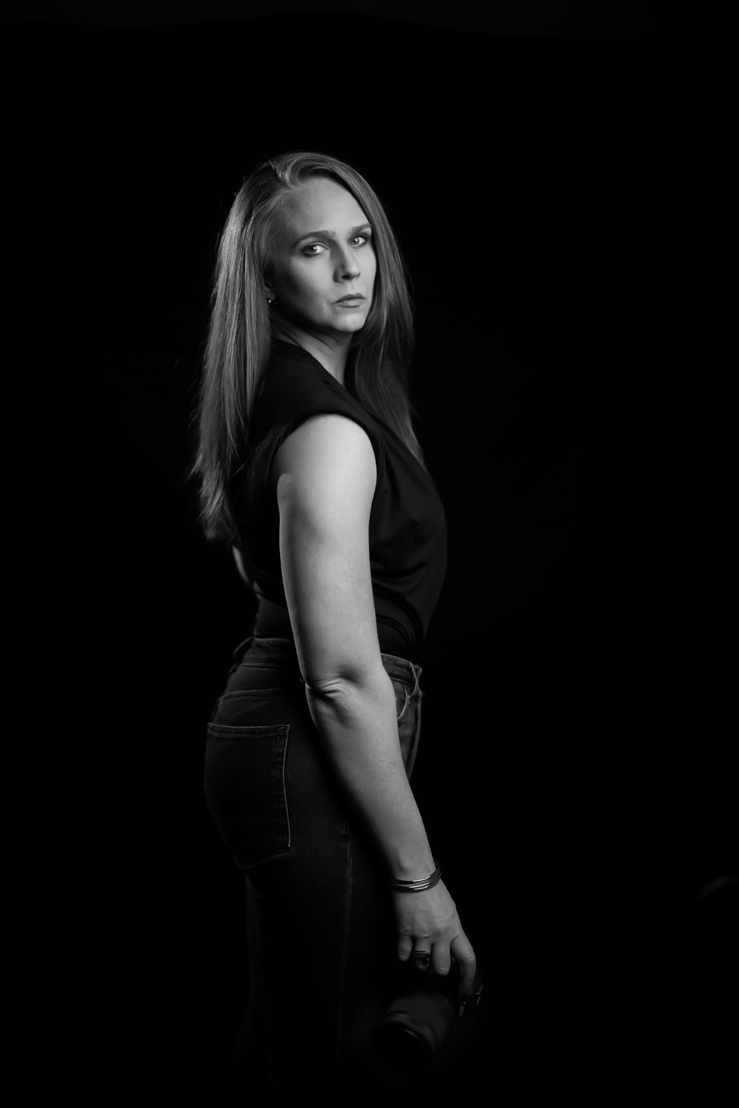 Striking black and white portrait in dramatic lighting with figure in dark attire against black background.
