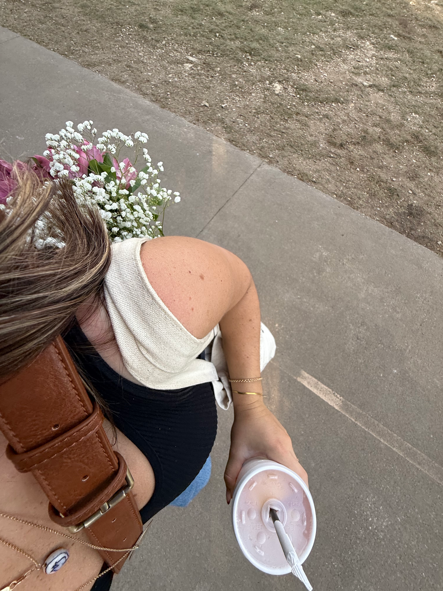 Overhead view of woman holding iced drink with flowers in her hair on a sidewalk.