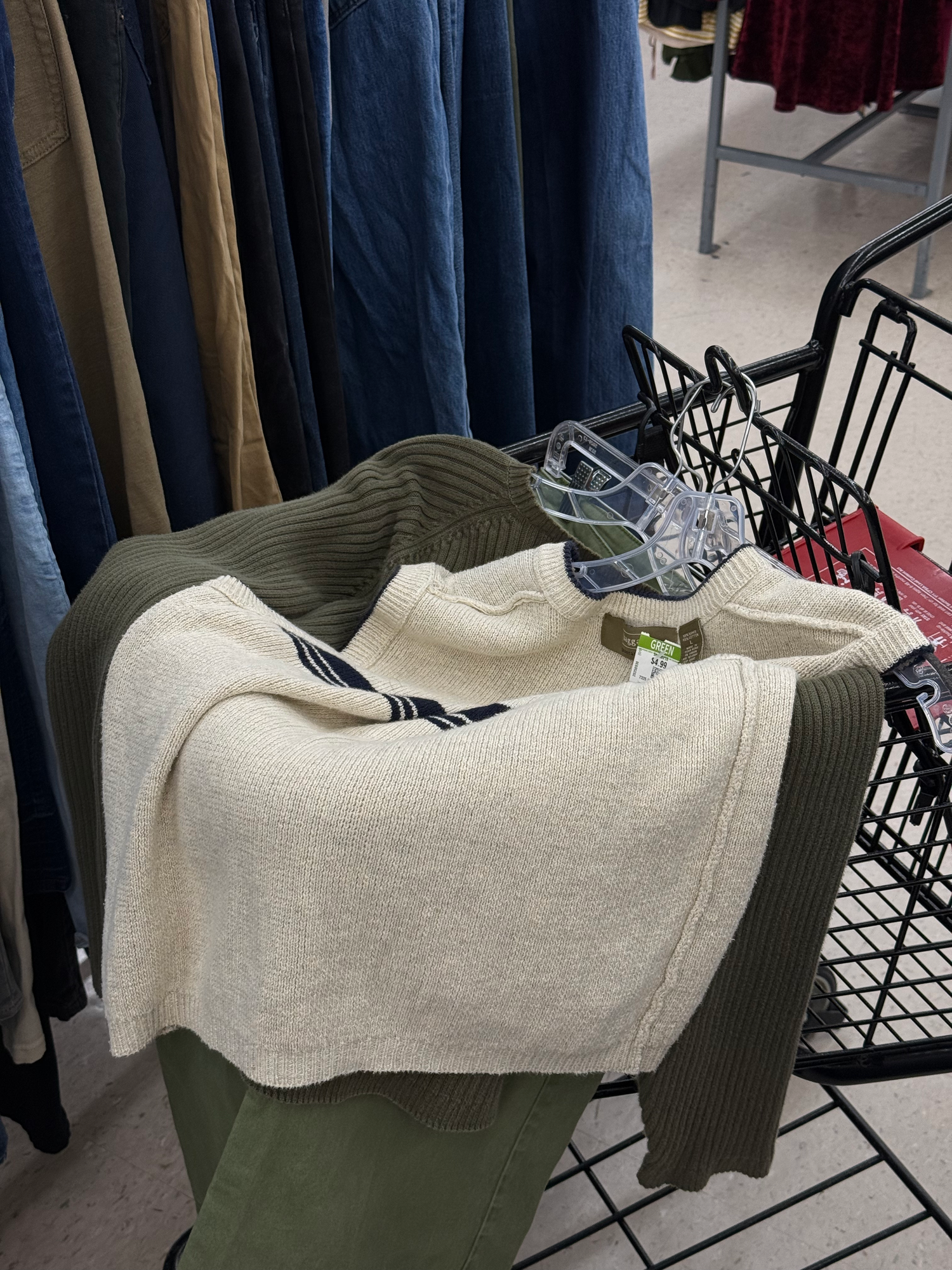 Cream knit sweater and olive green pants in a wire shopping cart at a thrift store.