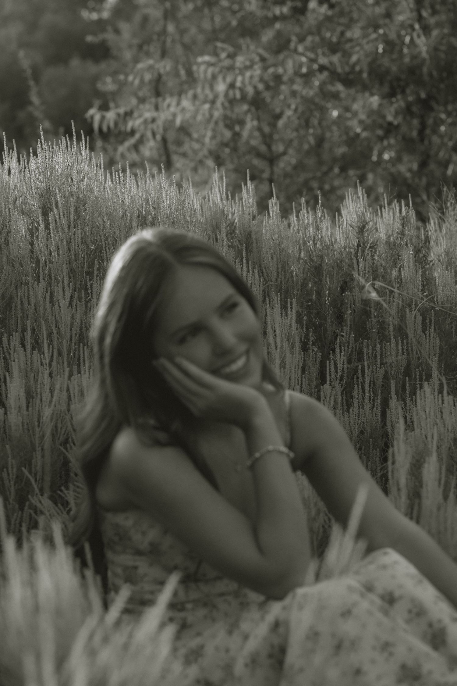 Young woman smiling while sitting in a wheat field in a soft black and white portrait photo.