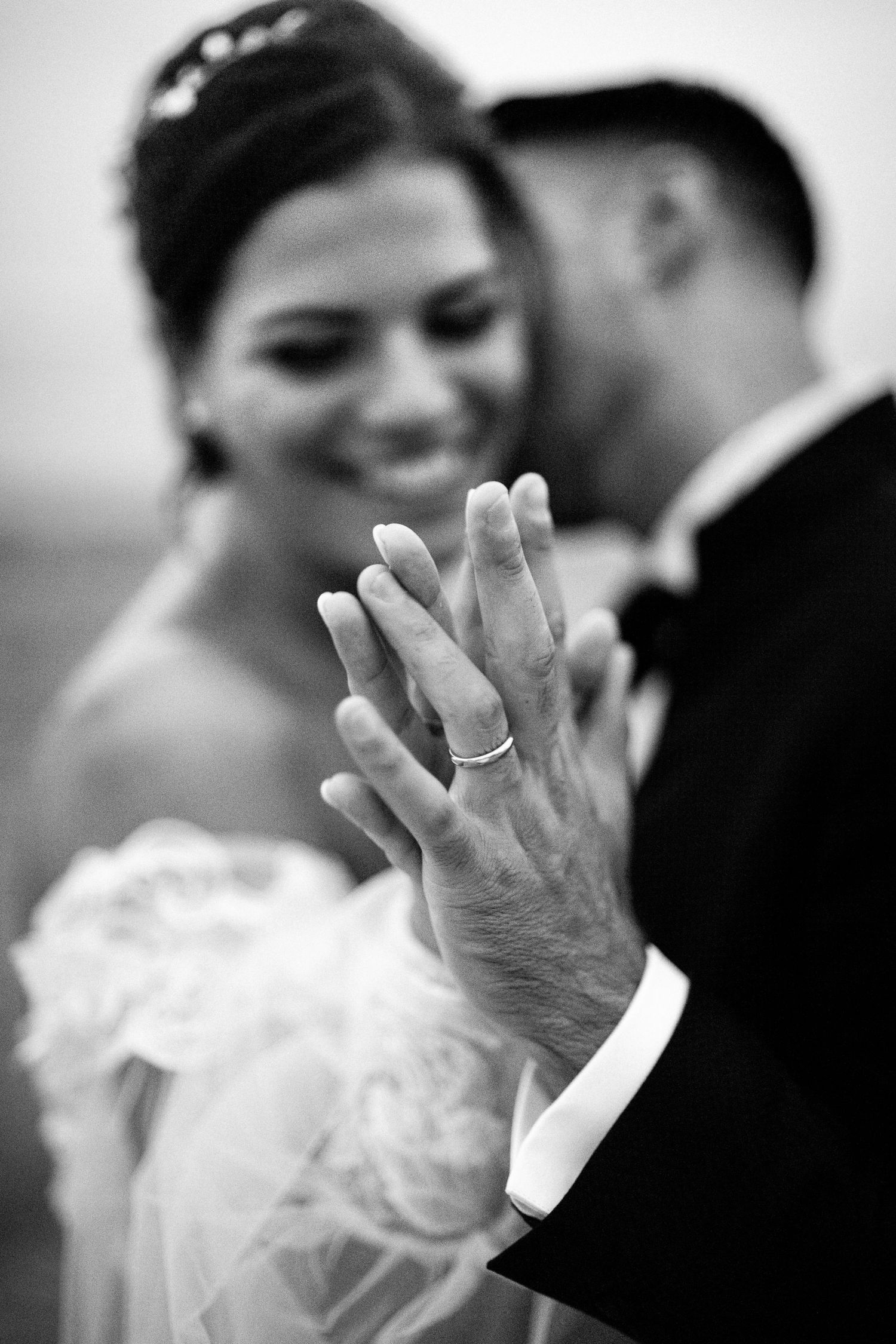 Black and white wedding photo of smiling bride and groom showing off their wedding rings.
