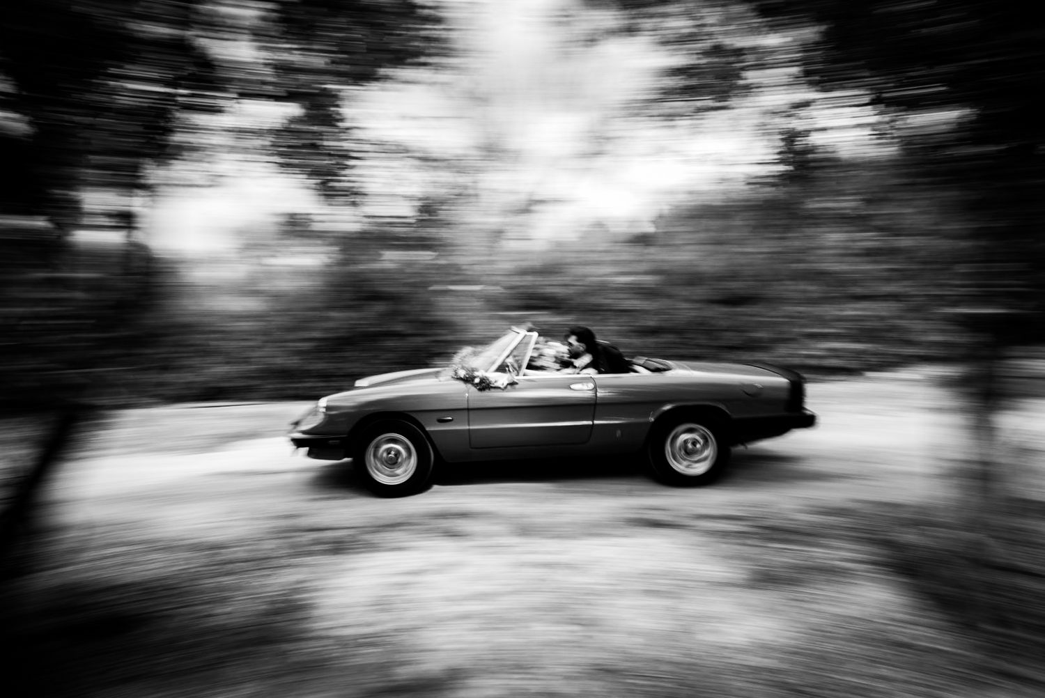 Classic sports car driving through a forest road in black and white motion blur photography.