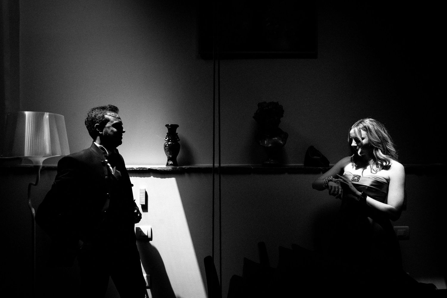 Black and white photo of a man and woman in formal attire conversing in a dramatically lit room.