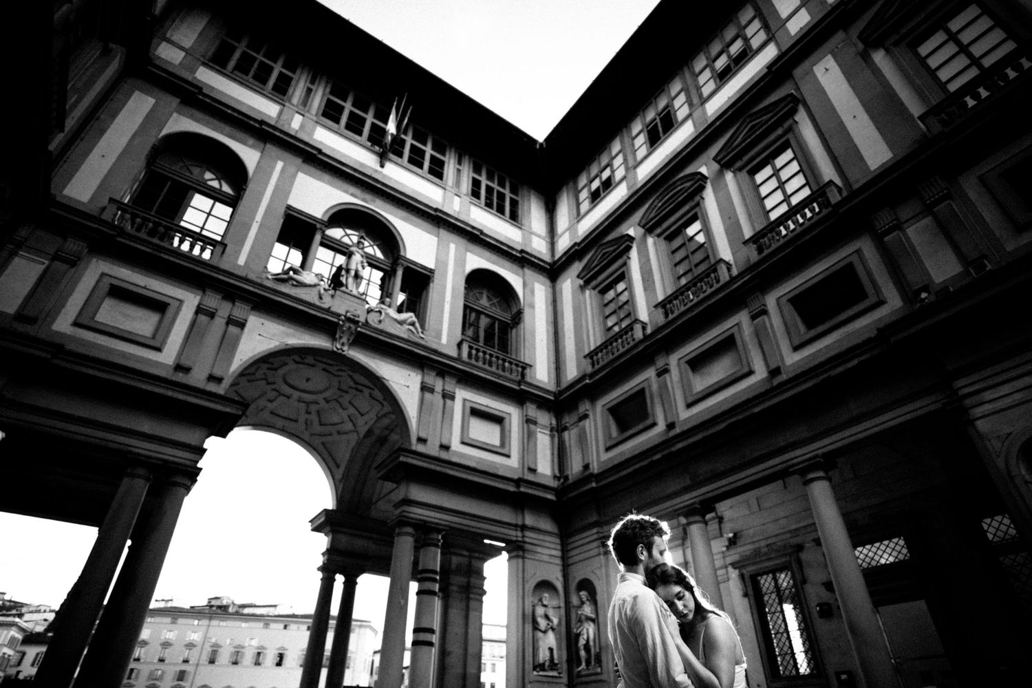 Black and white photo of a couple embracing in the courtyard of the Uffizi Gallery in Florence, Italy.