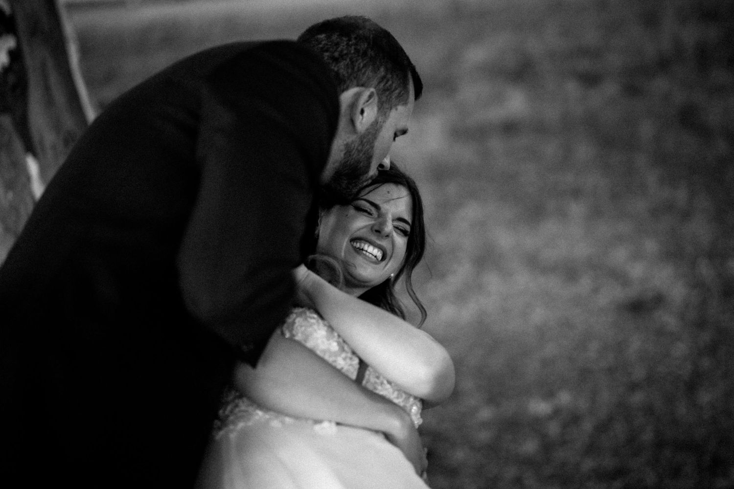Black and white photo of a romantic moment between newlyweds sharing a joyful embrace at their wedding.
