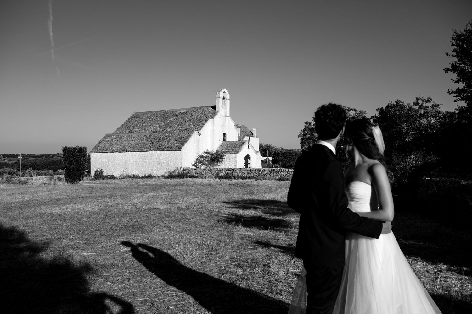 A series of black and white photos showing a couple walking near a small white church in a rural landscape.