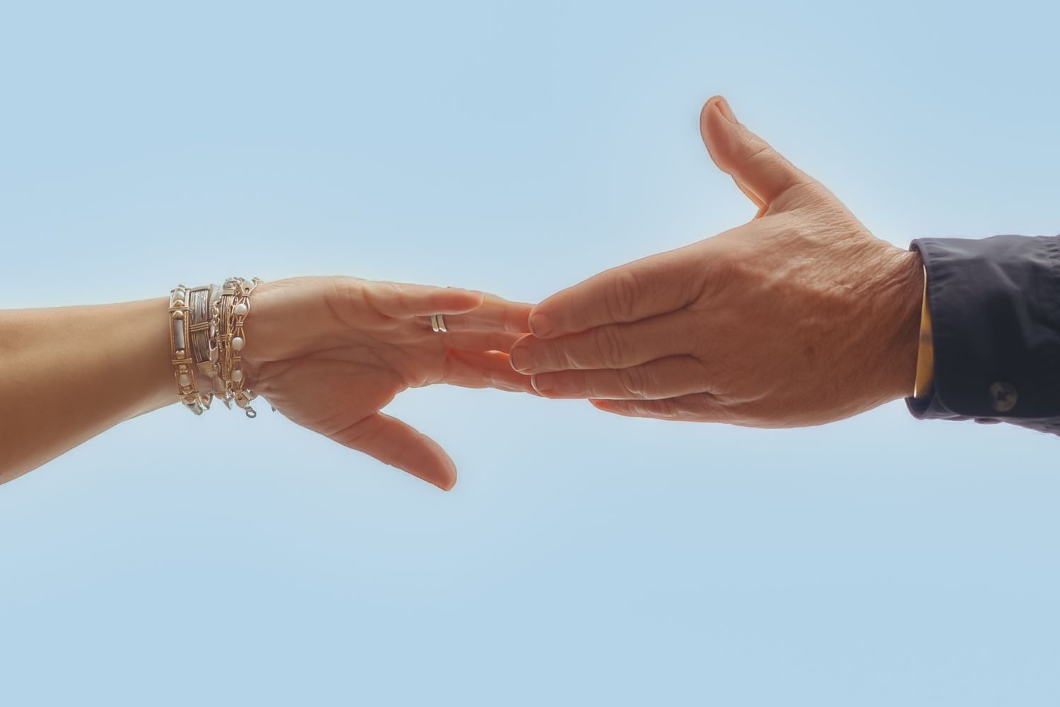 Two hands reaching towards each other against a bright blue sky background in a series of sequential images.
