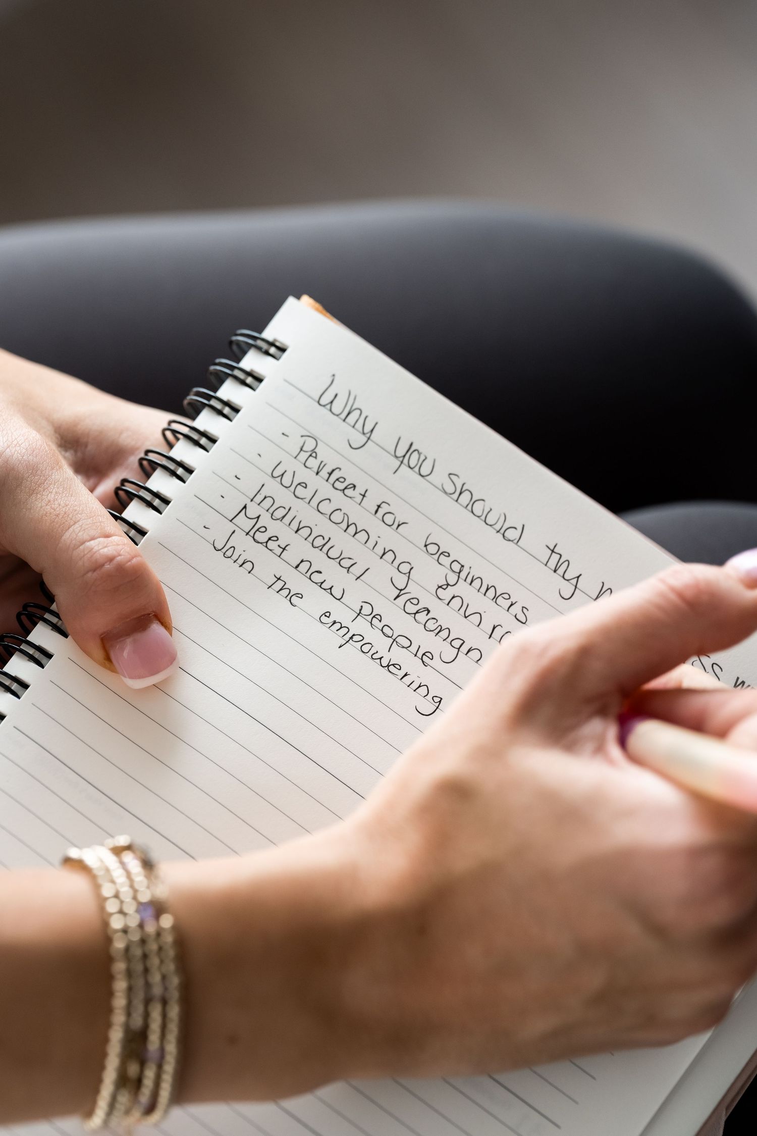 Hands holding a spiral notebook with handwritten list titled Why You Should Try, with bracelets visible on wrist.