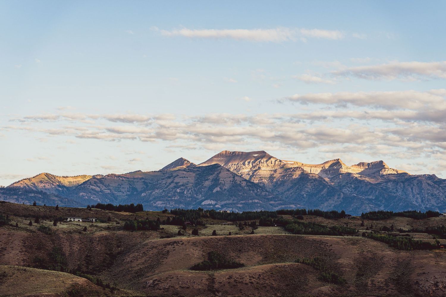 Rocky mountain range with rugged peaks silhouetted against cloudy sunset sky.