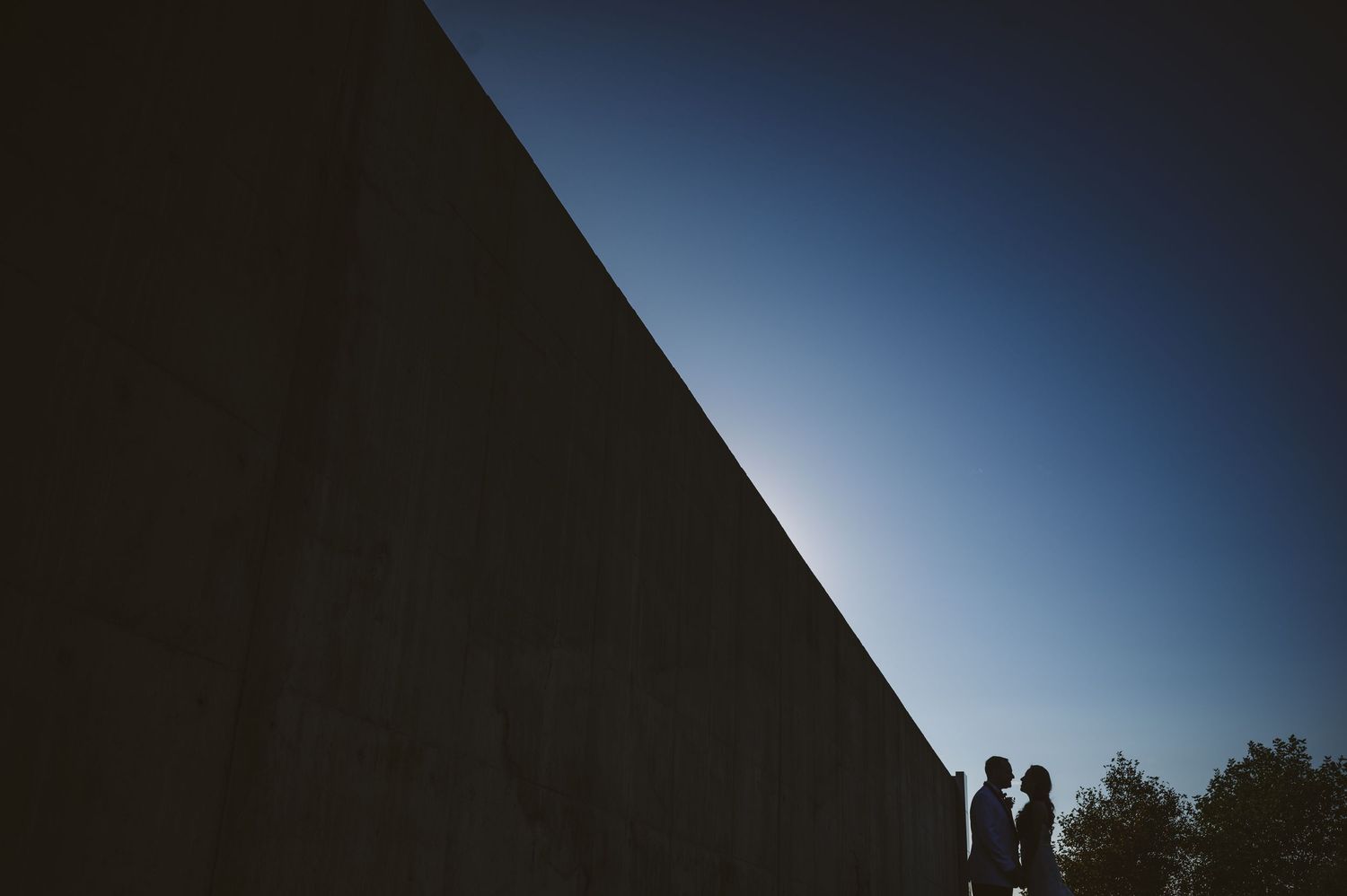 Romantic silhouette of a couple against a dramatic sunset sky with city skyline in the background.