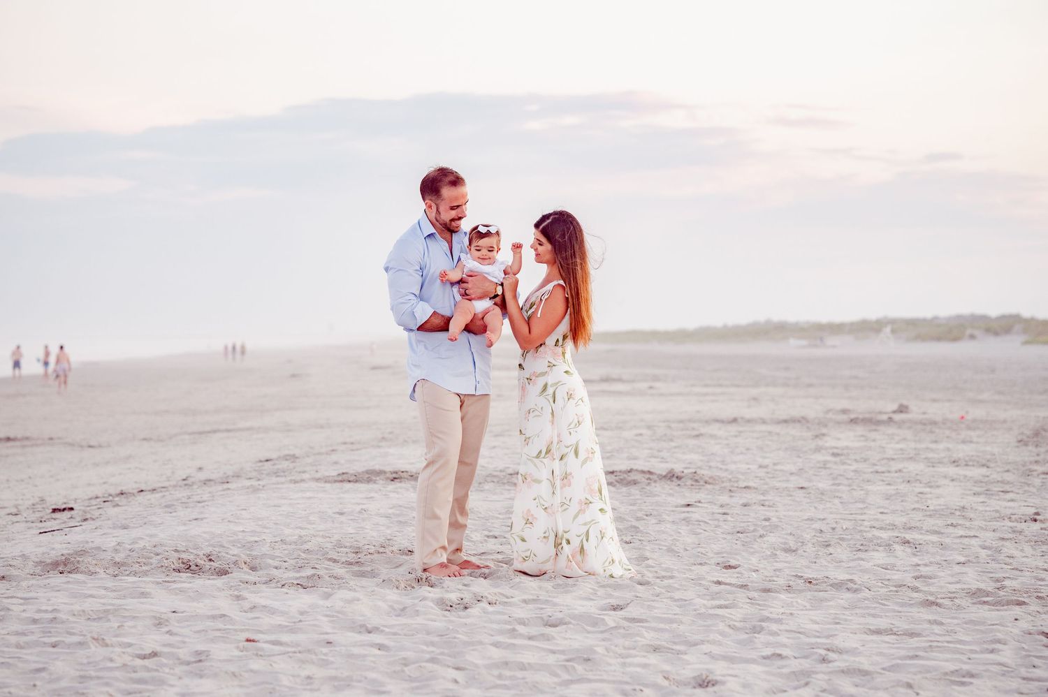 Family walking along peaceful beach at sunset in flowing summer attire.