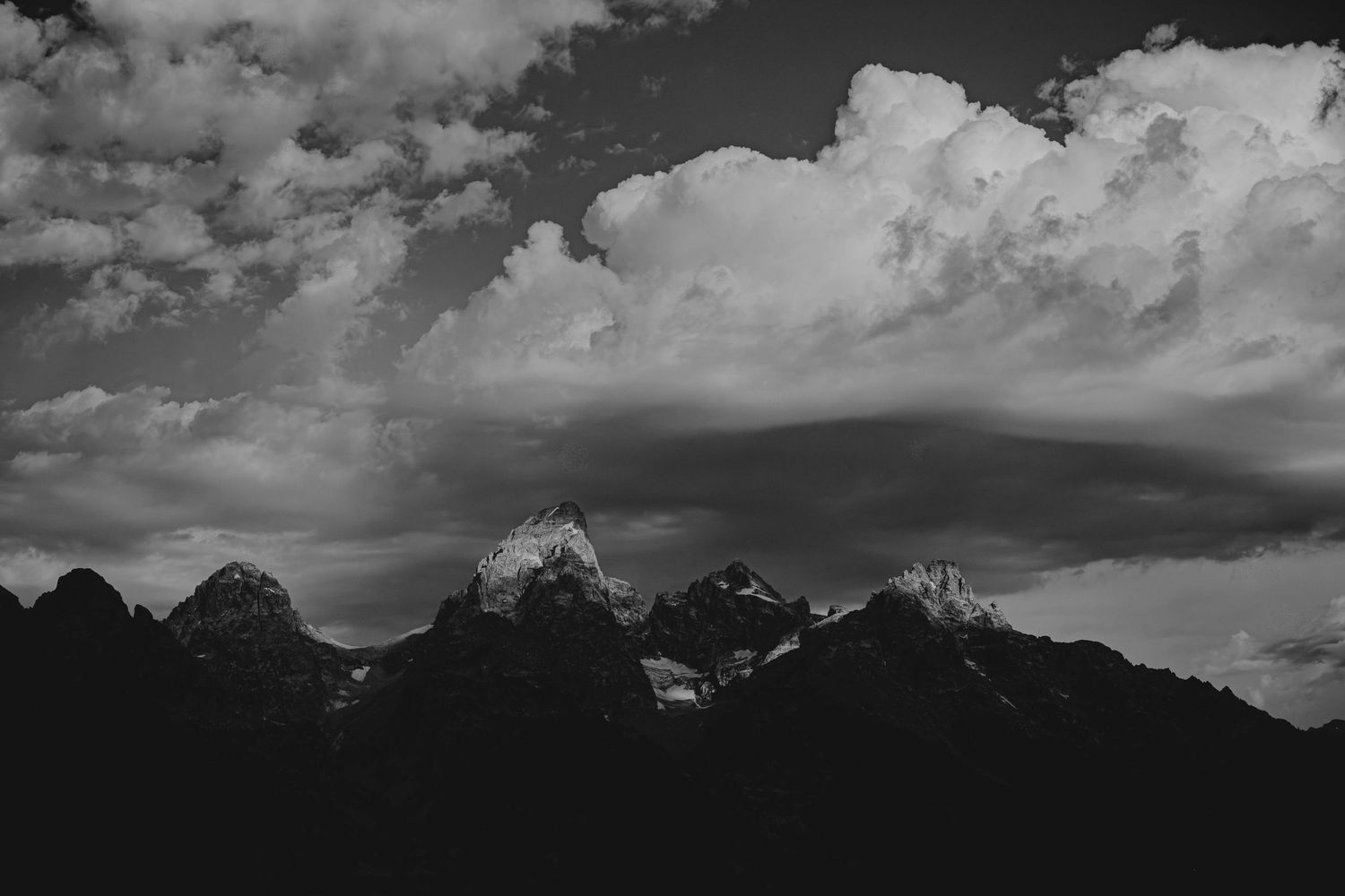 Black and white panoramic mountain landscape with dramatic cloud formations above peaks.