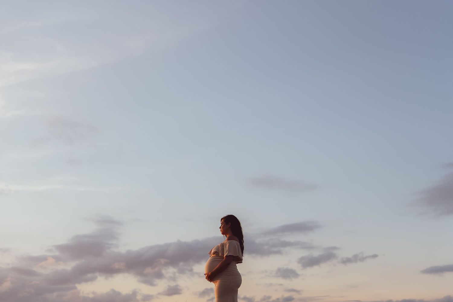 A silhouette of an expectant mother against a dusky sky.