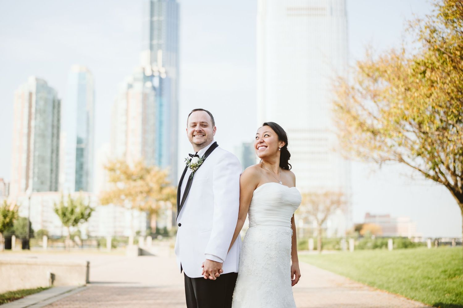 Wedding couple posing with Manhattan skyline visible through autumn trees.