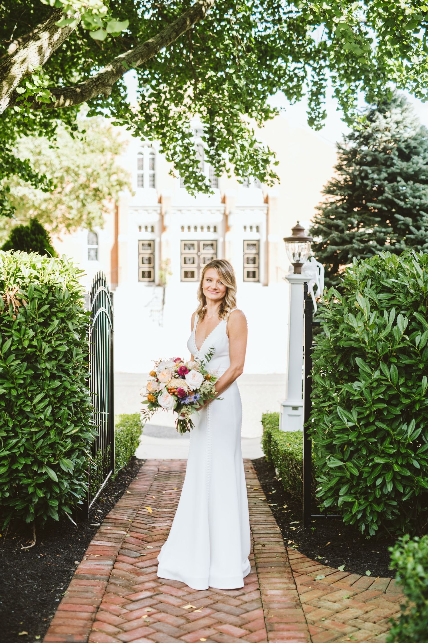 White wedding dress against brick pathway lined with lush green garden foliage.