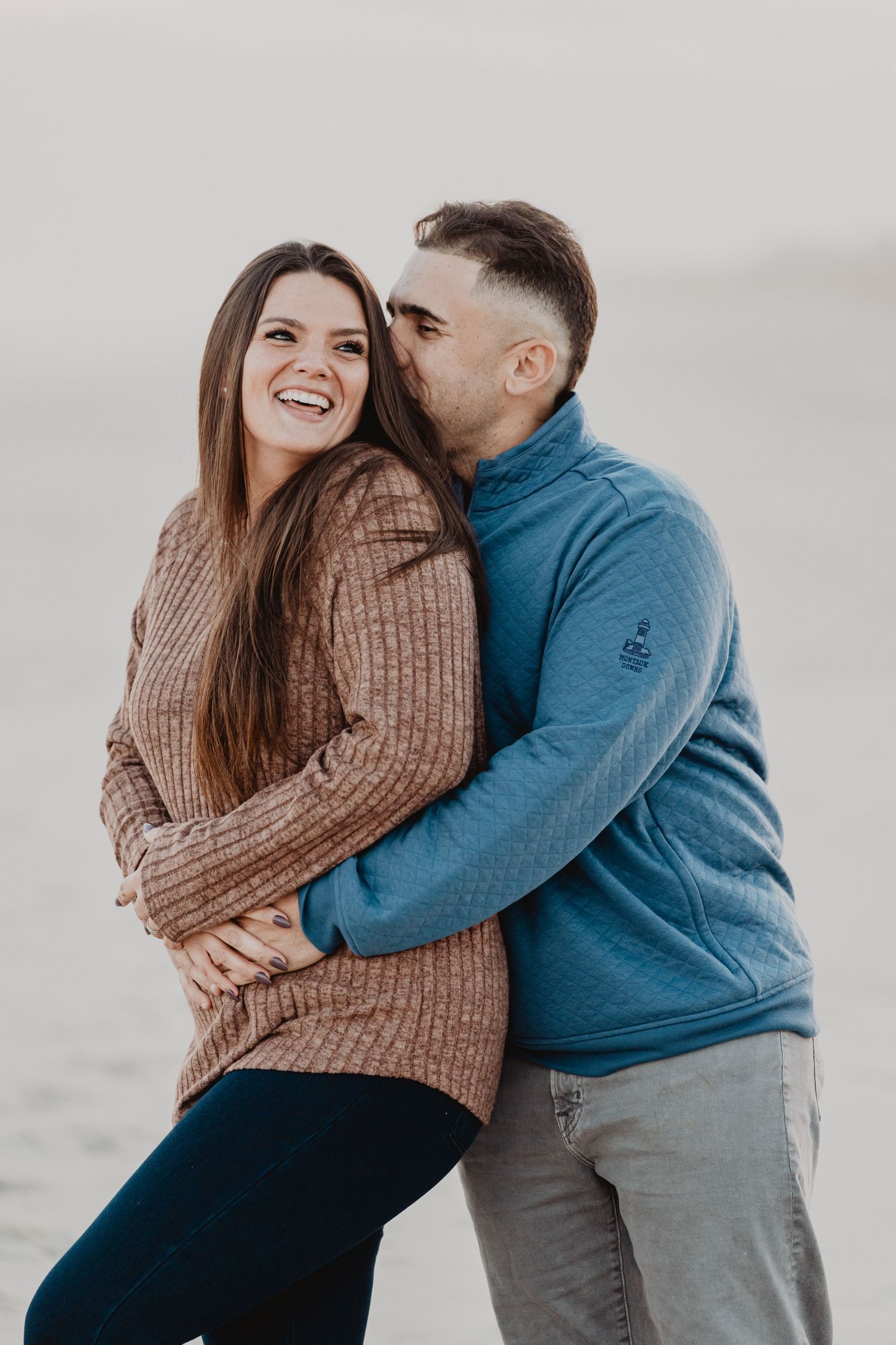 A couple in casual winter attire sharing intimate moments and embracing on a cloudy day.
