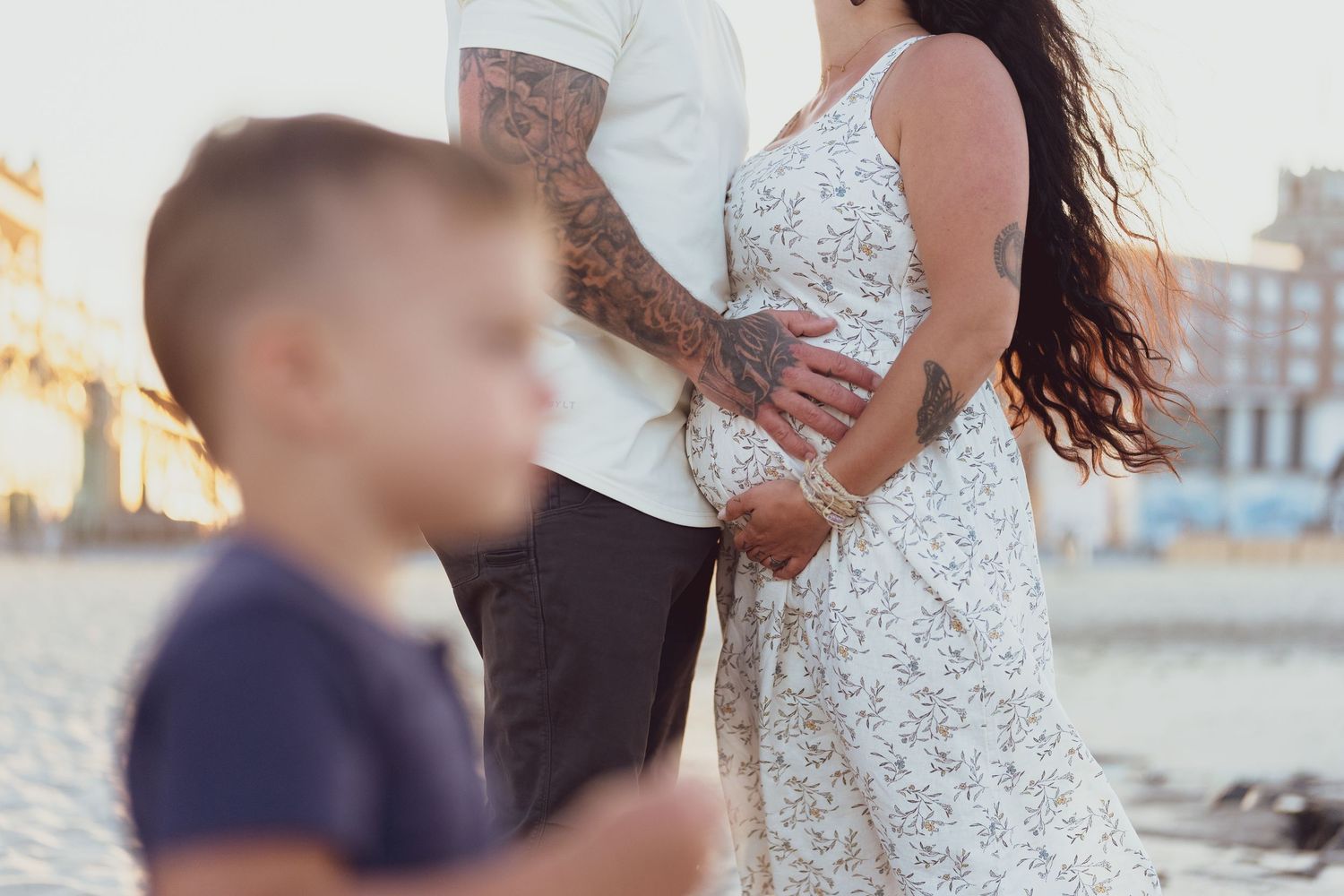 A couple in white and dark clothing standing together on a beach at sunset.